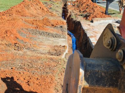 an image with a backhoe bucket in the foreground slightly obscuring a trench with blue metallic tape